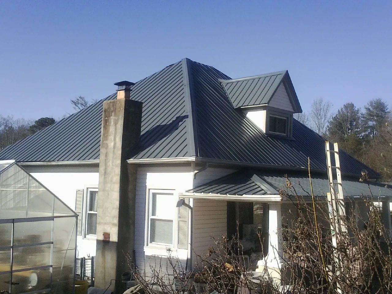 Dark blue standing seam metal roof on a white farmhouse with dormer — Slate & Tile Roof Repair by Roofing Brothers in Norwalk