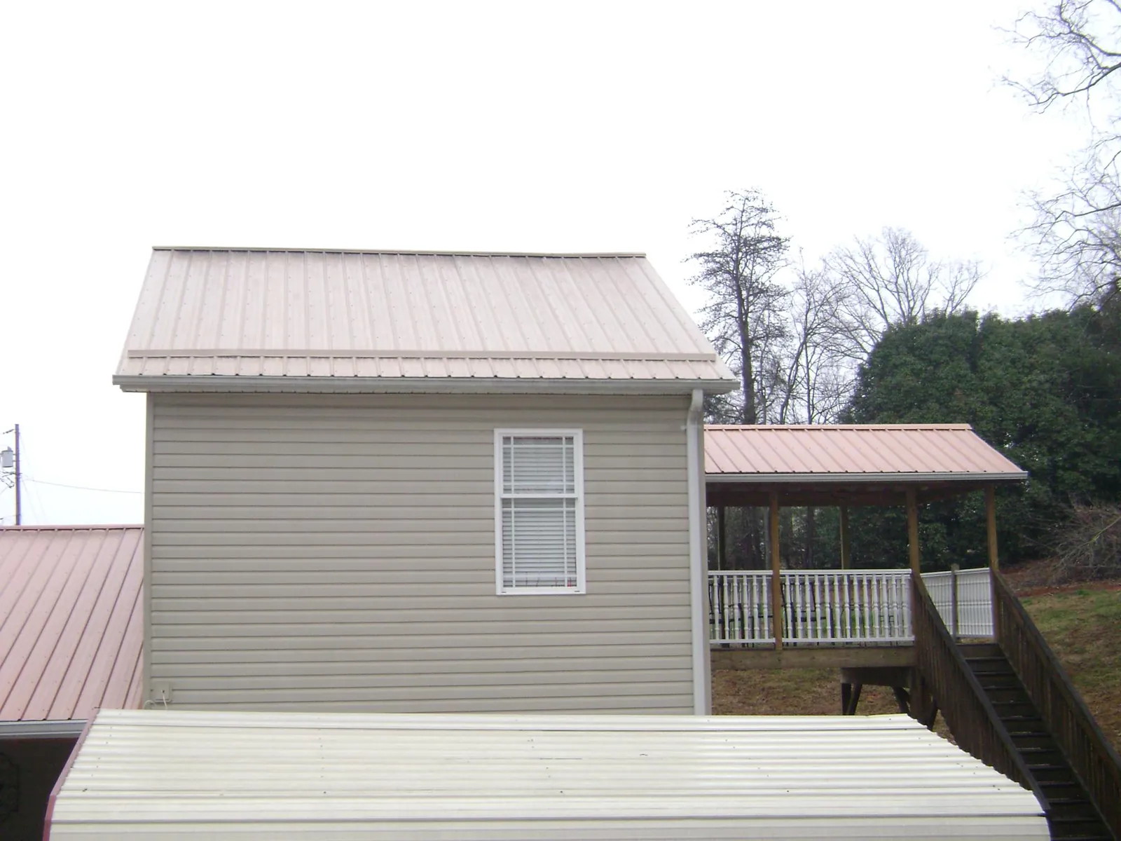 Tan metal roofs on a two story addition and attached porch, from a Roof Replacement job in Norwalk