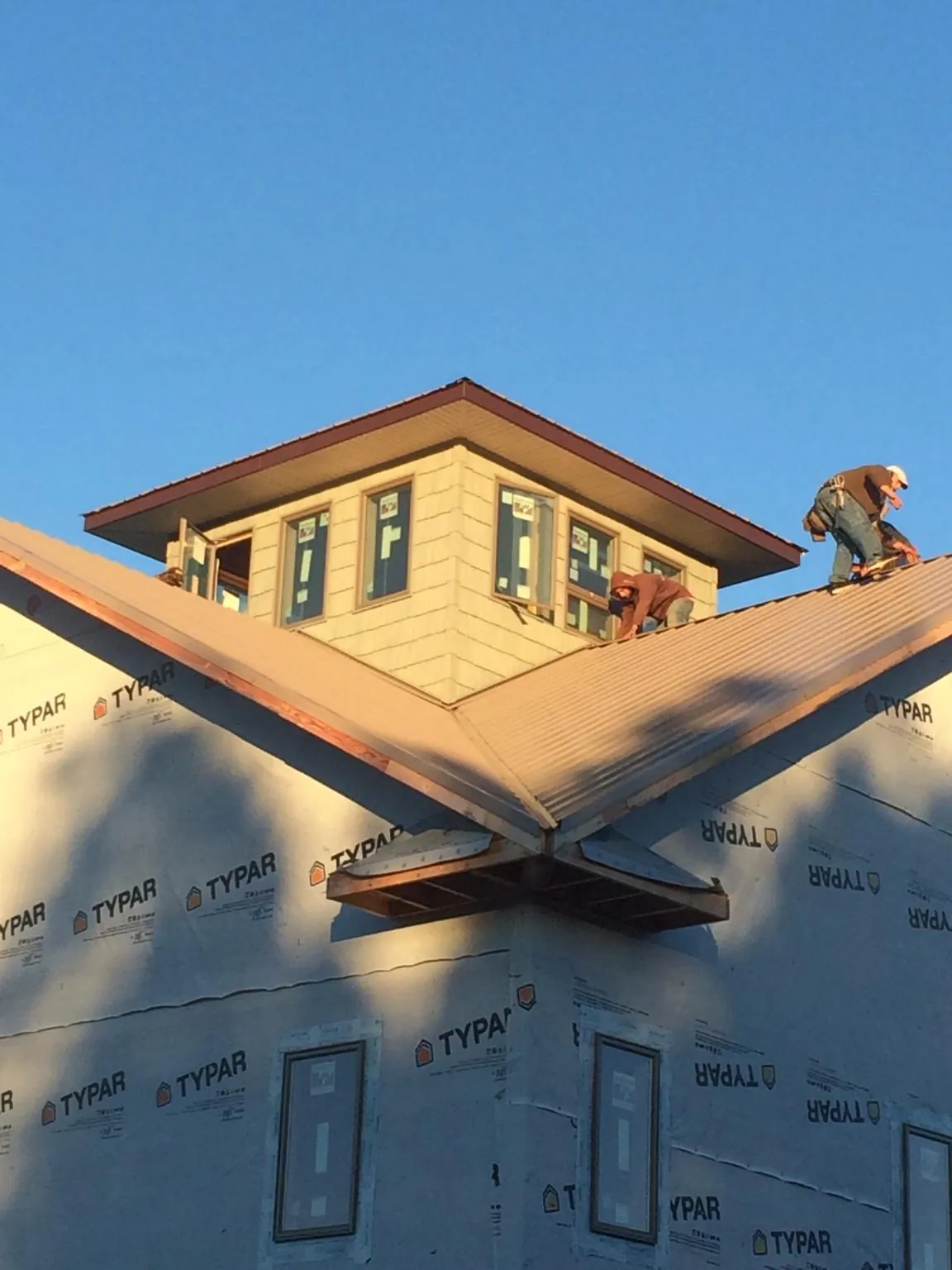 Roofers working around a rooftop cupola on a new metal roof at sunset — Roof Waterproofing in Norwalk by Roofing Brothers